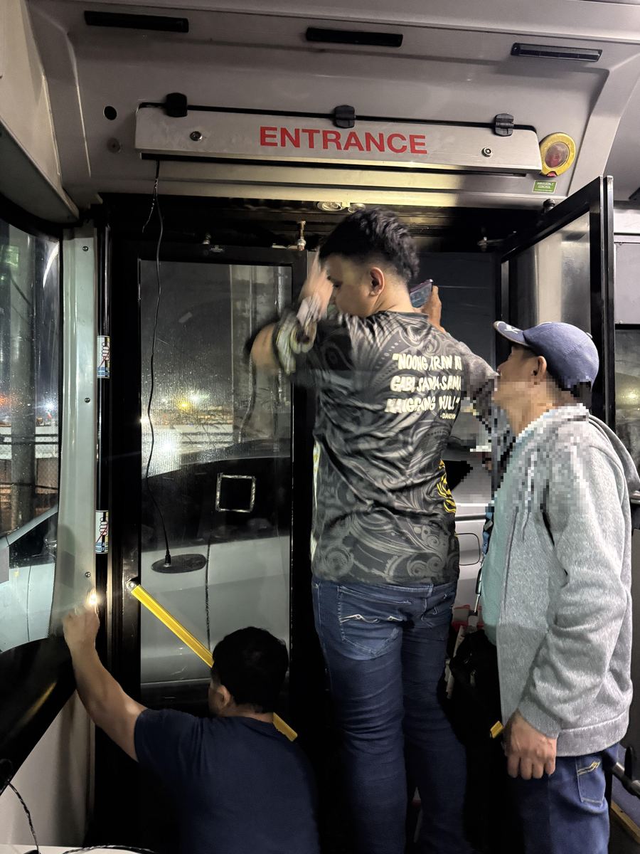 InfraLinx technicians installing a camera unit above the entrance door of a bus, at night.